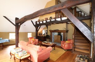 Un salón espacioso con techo de madera alto, chimenea y una escalera que conduce a un nivel superior.