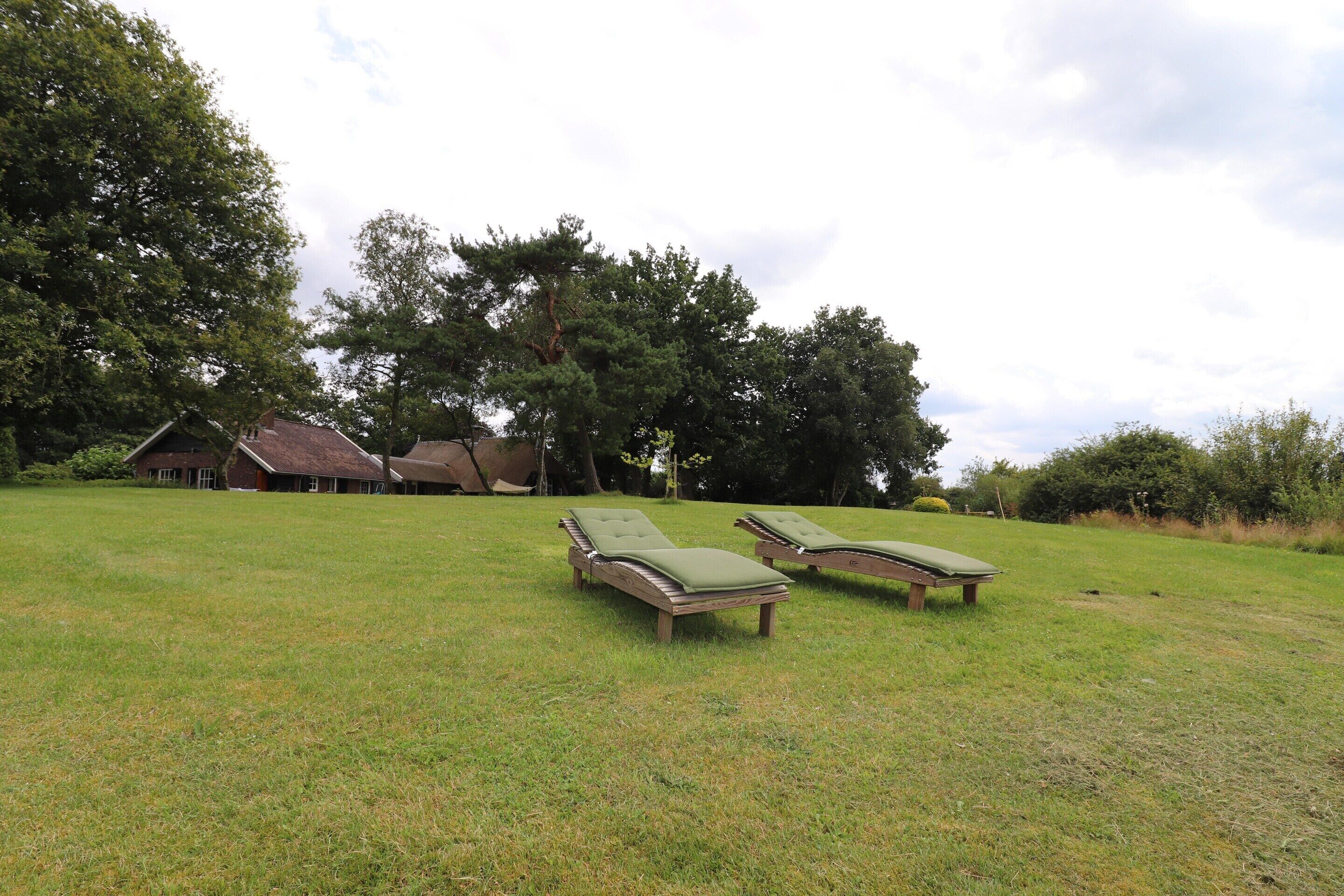 A grassy area with two wooden lounge chairs and a rustic building in the background.
