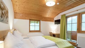 Ein Schlafzimmer mit Holzbalkendecke, einem Bett mit weißen Leinen, einem Schreibtisch mit Lampe und einem Fenster mit Vorhängen.