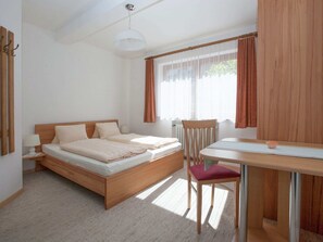Une chambre à coucher avec un lit en bois, un bureau, une chaise et une fenêtre avec des rideaux.