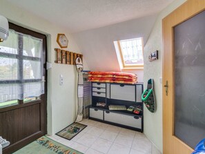A compact room with a window, a door, a small shelf with folded blankets, a radiator, and a mat on the floor. - Cozy Apartment in Lichtenhain With Garden (Sebnitz)