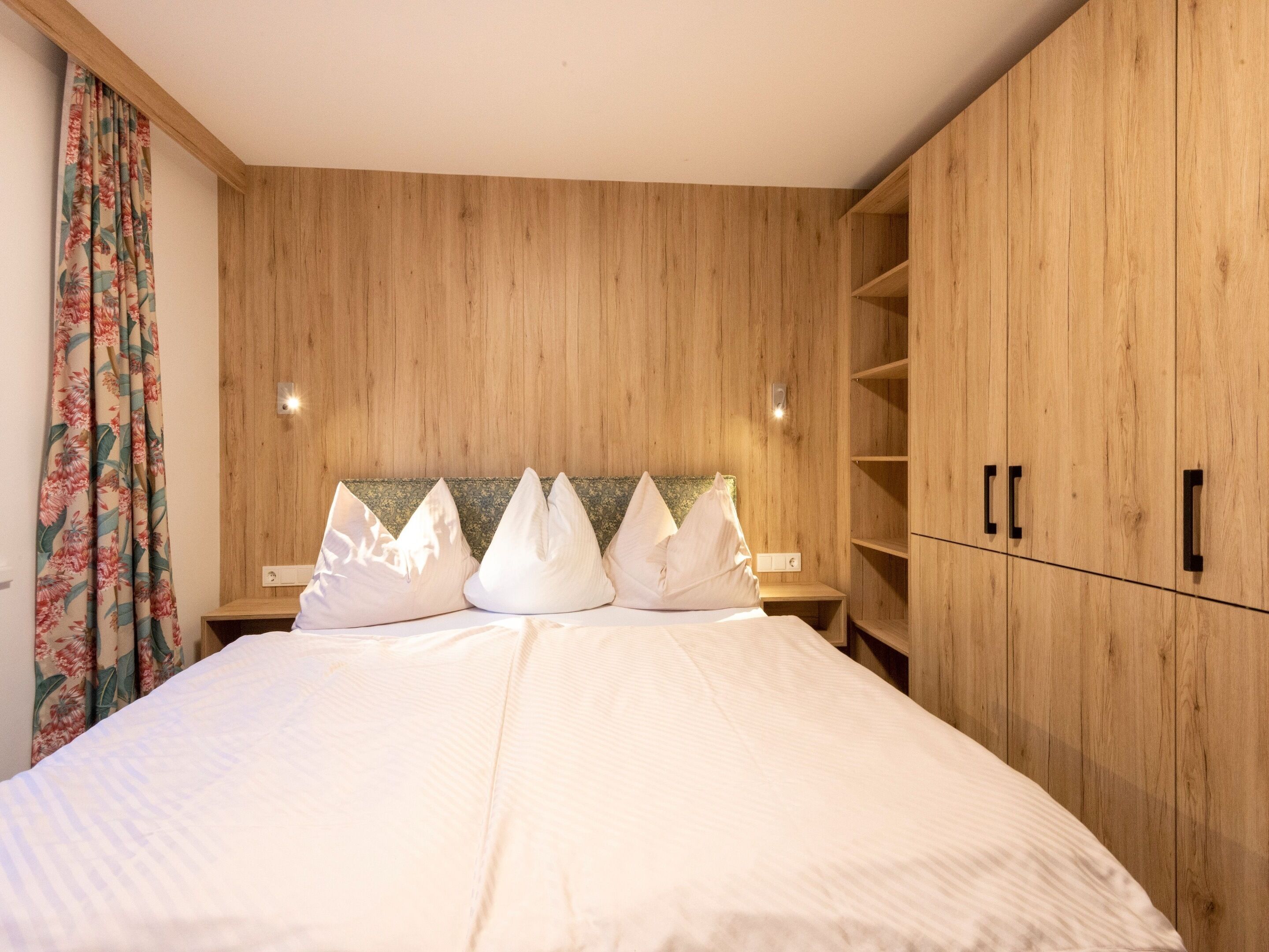 Een slaapkamer met een houten hoofdbord, een bed met witte beddengoed en een nachtkastje met een lamp.
