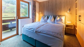 A bedroom with a large bed, wooden walls, a view of a green landscape through a sliding door, and a small bedside table. - Apartment in Wald Near Zillertal Ski Area (Wald im Pinzgau)