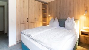 A bedroom with a bed, wooden wardrobe, and a nightstand with a lamp. - Apartment in Wald Near Zillertal Ski Area (Wald im Pinzgau)