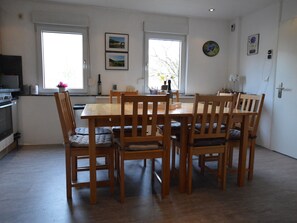 A dining area with a wooden table and chairs, a window with a view, and a kitchen area with appliances.
