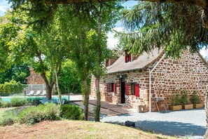 Ein Gebäude aus Stein mit roter Tür, einem Pool und einem Garten.