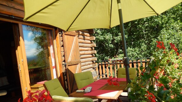 An outdoor seating area with wooden tables and chairs, a yellow umbrella, and a wooden fence. - Spacious Chalet for 4 in Hommert (Hommert)