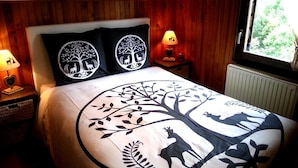 A bedroom with a wooden headboard, a large bed with a tree and deer design, two nightstands with lamps, and a window with a view of greenery. - Spacious Chalet for 4 in Hommert (Hommert)