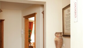 A hallway with a wooden door leading to a room, a large vase on a wooden dresser, and a framed document on the wall. - Chalet in Saalbach With Sauna (Saalbach-Hinterglemm)