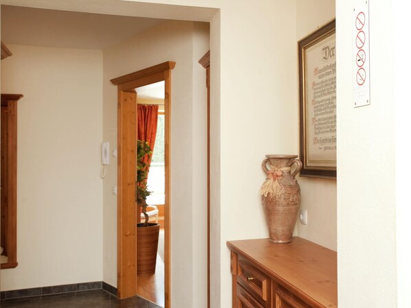A hallway with a wooden door leading to a room, a large vase on a wooden dresser, and a framed document on the wall. - Chalet in Saalbach With Sauna (Saalbach-Hinterglemm)