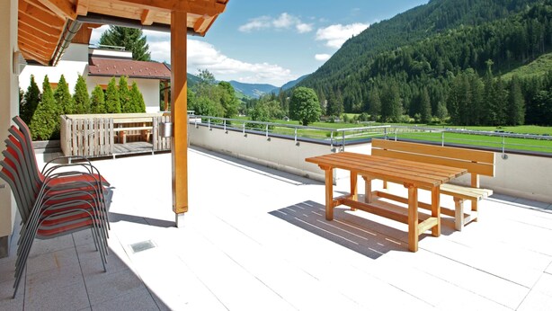 A covered outdoor area with wooden furniture, including a table and chairs, overlooking a mountainous landscape. - Chalet in Saalbach With Sauna (Saalbach-Hinterglemm)