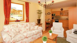 A living room with a sofa, a coffee table, and a dining area with chairs. There is a kitchen in the background with wooden cabinets and a microwave. - Chalet in Saalbach With Sauna (Saalbach-Hinterglemm)
