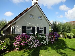 A house with a gabled roof, two windows with shutters, and a well-maintained garden with various flowers. - Holiday Home in Steendam by Schild Lake (Steendam)