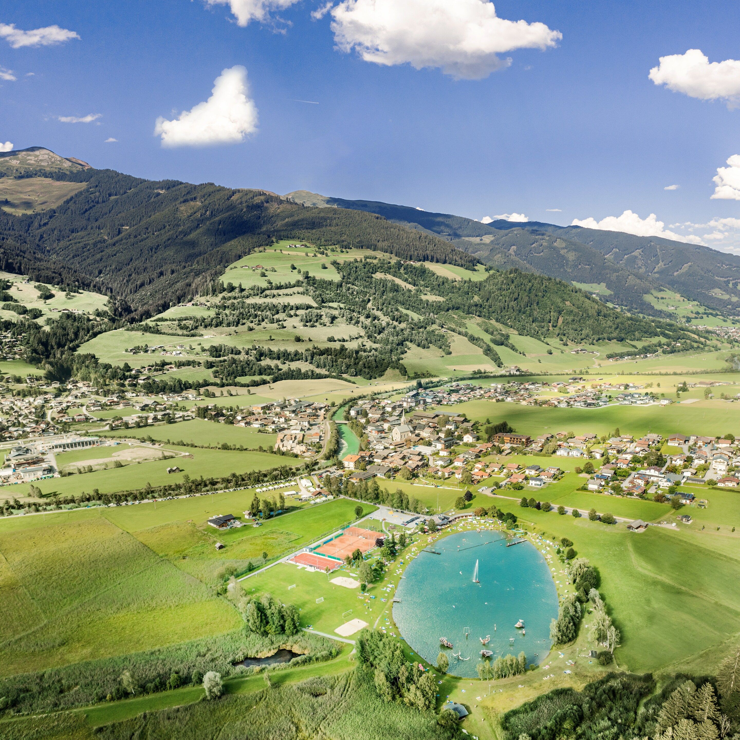 Un pueblo con un lago central, rodeado de colinas y montañas verdes.
