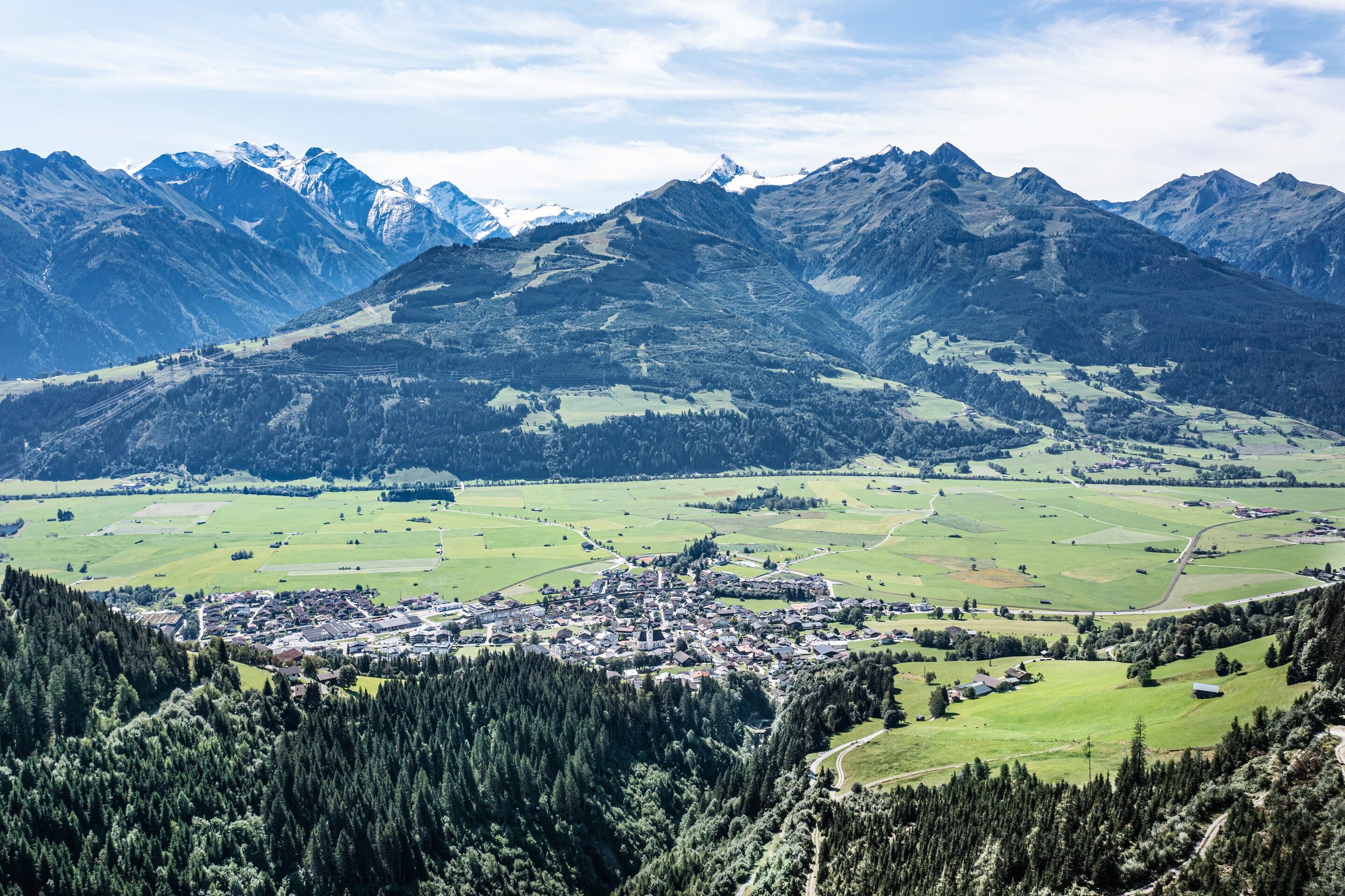 A mountainous landscape with a town nestled in a valley, surrounded by forests and fields.