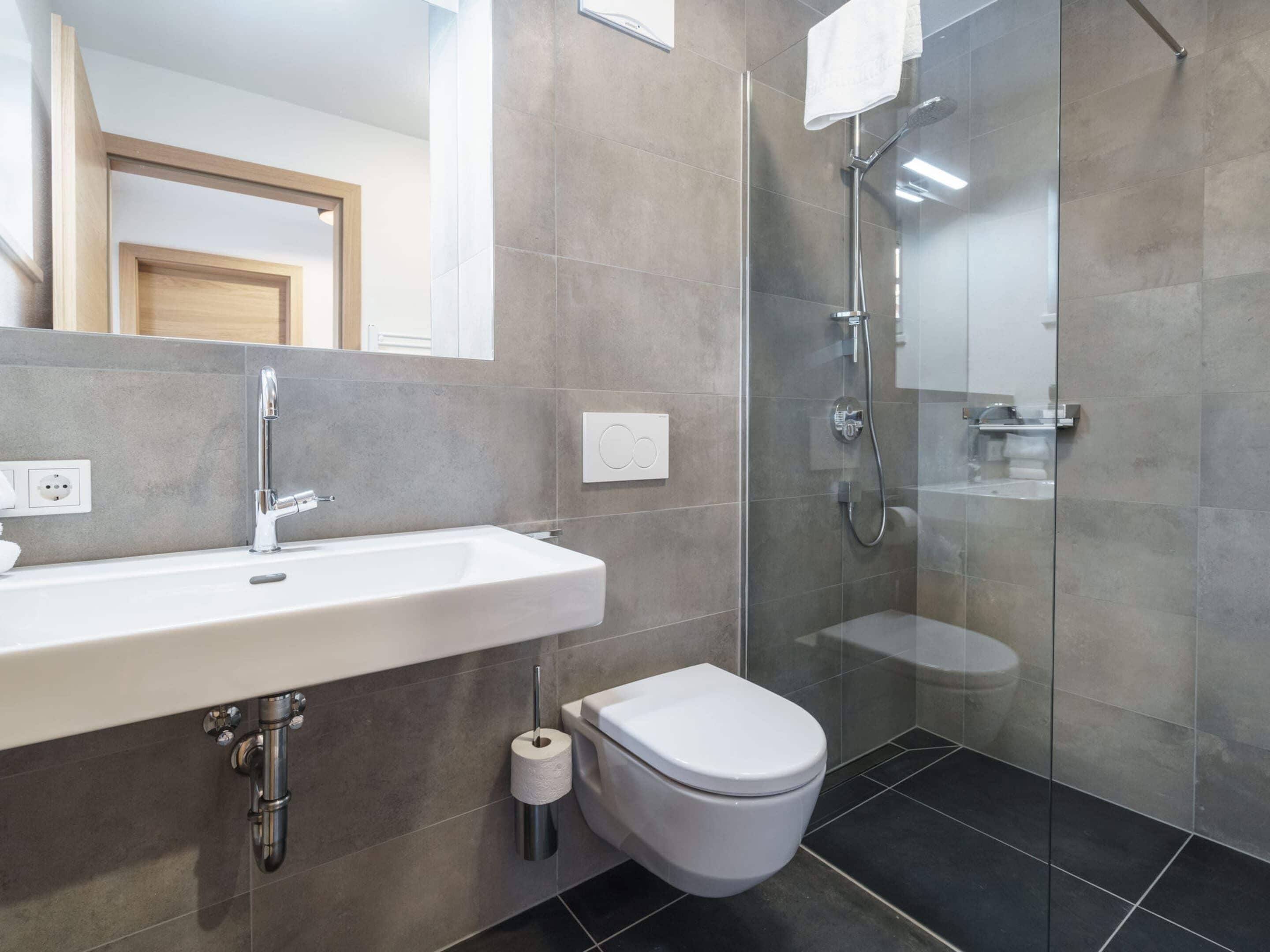 A modern bathroom with a white sink, a toilet, and a glass-enclosed shower area.