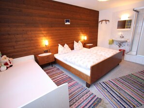 A bedroom with a wooden headboard, a white bed, a bedside table with a lamp, a small bedside table with a mirror, a bathroom with a sink and shower, and a colorful striped rug. - Spacious Apartment near Ski Area in Salzburg (Dienten am Hochkoenig)