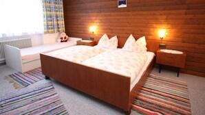 A bedroom with a wooden headboard, two bedside tables with lamps, a window with curtains, a radiator, and a colorful striped rug. - Spacious Apartment near Ski Area in Salzburg (Dienten am Hochkoenig)