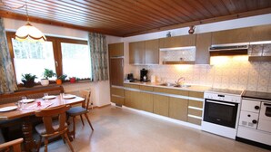 A kitchen with wooden cabinets, a dining table with chairs, a built-in oven, and a window with curtains. - Spacious Apartment near Ski Area in Salzburg (Dienten am Hochkoenig)