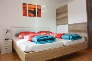 Uma cama de solteiro com estrutura de madeira, cabeceira branca e mesa de cabeceira com abajur.
