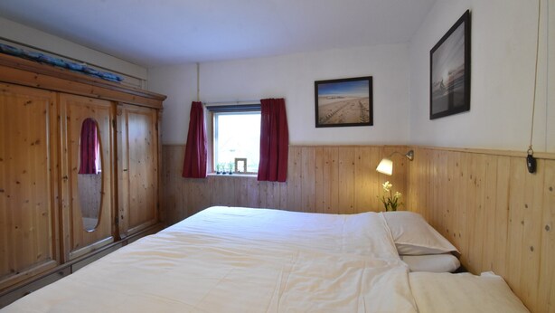 A bedroom with a large bed, wooden wardrobe, a window with curtains, and a framed picture on the wall.