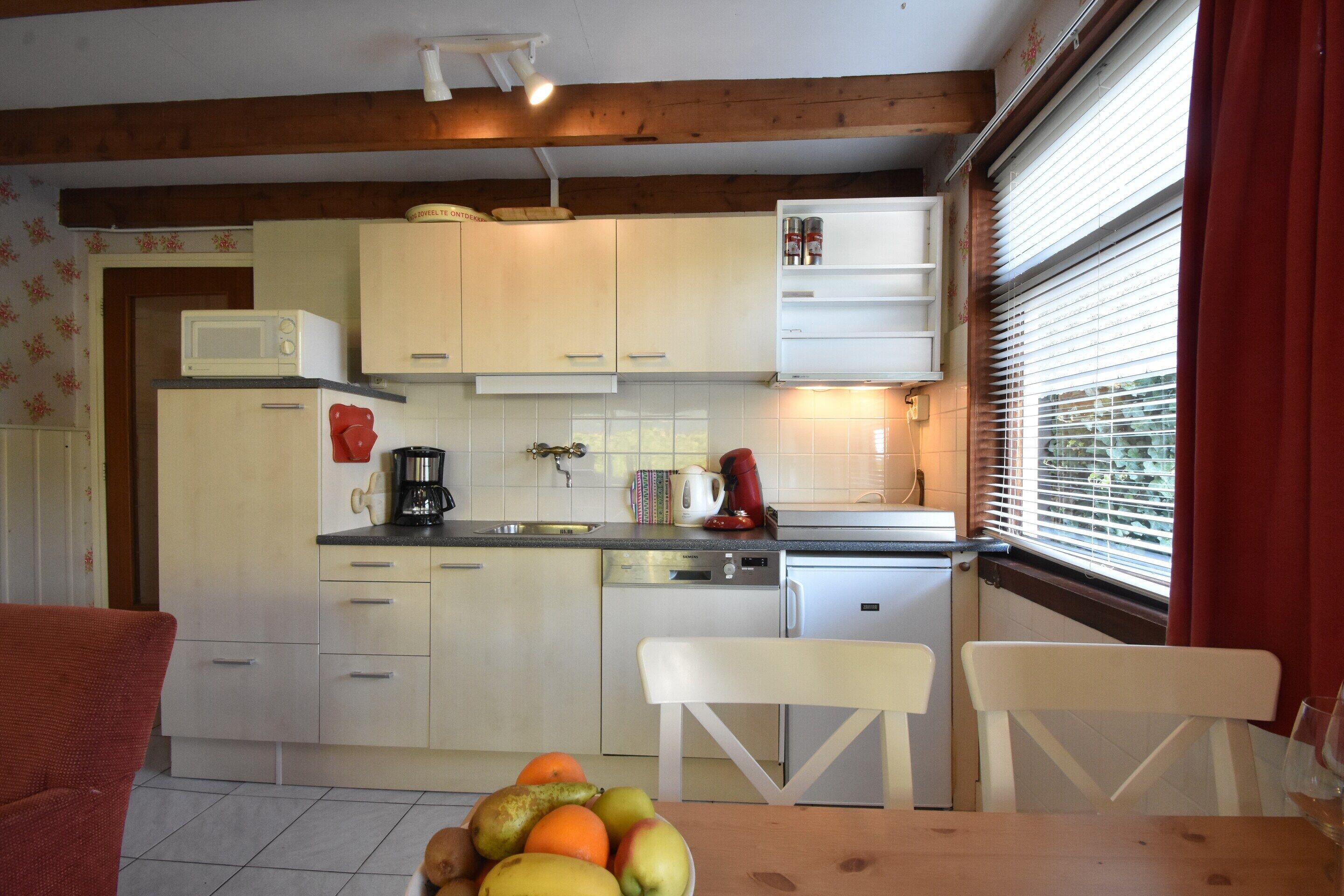 Une cuisine avec des meubles blancs, un four à micro-ondes, une machine à café et un panier de fruits sur la table.
