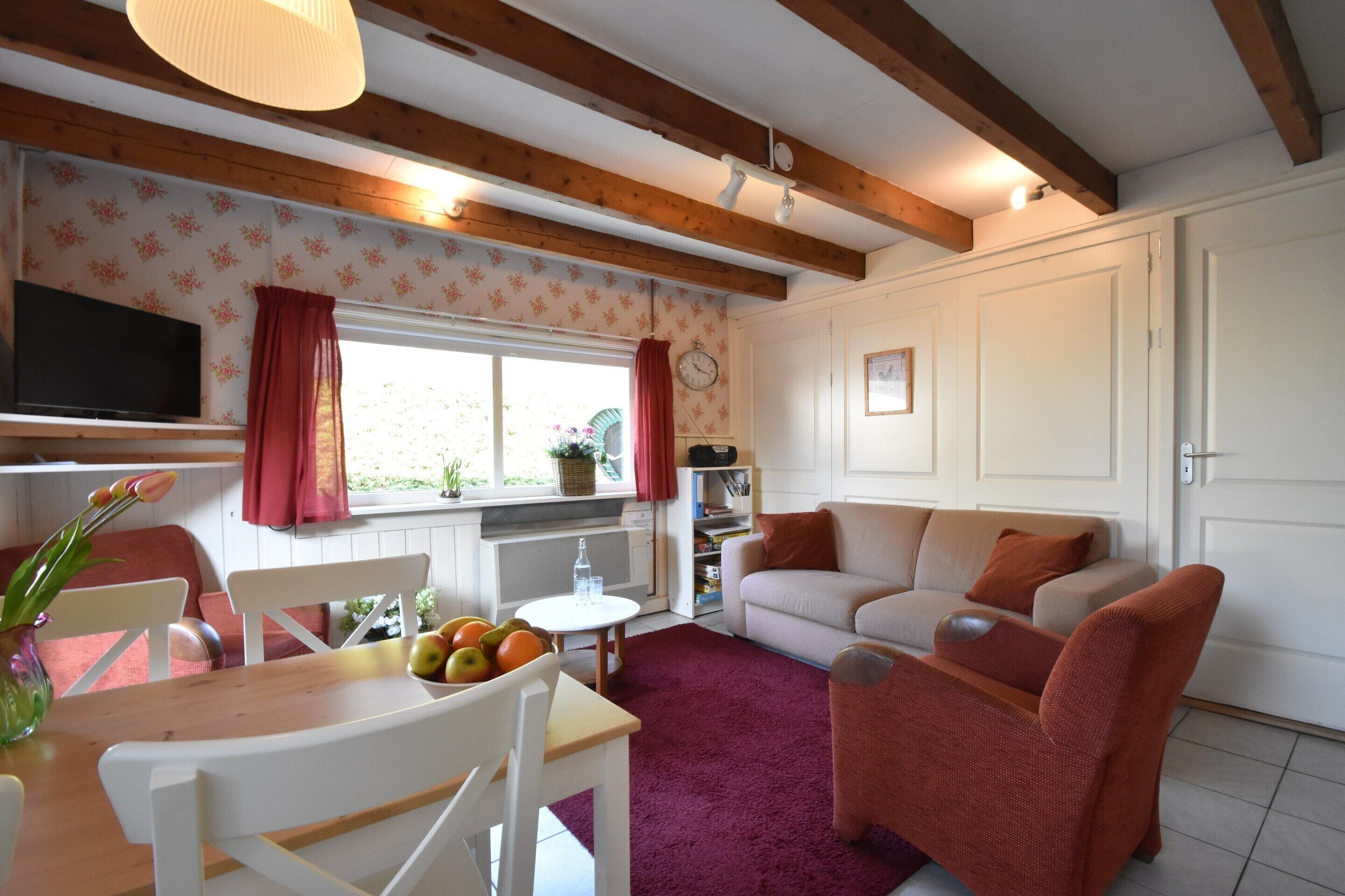 A cozy living room with a wooden ceiling, a sofa, a TV, and a dining area with a table and chairs.