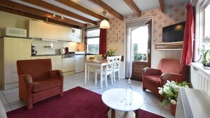 A cozy living room with a red sofa, a white dining table, and a kitchen area with wooden beams and a TV.