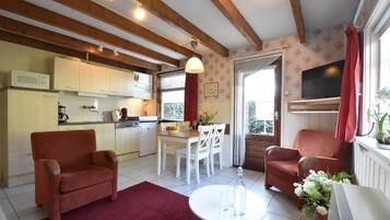 Una sala de estar acogedora con un sofá rojo, una mesa de comedor blanca y una cocina con vigas de madera y un televisor.
