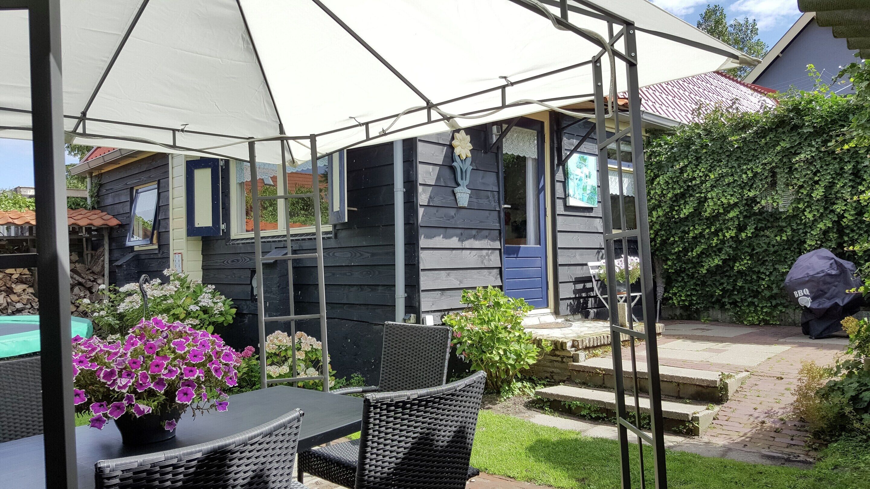 Een overdekt terras met tuinmeubilair, een zwembad en een huis op de achtergrond.