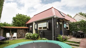 A house with a red-tiled roof, a black exterior, and a small front yard with a trampoline and a patio table.