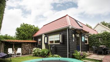 Una casa con techo de tejas rojas, fachada negra y un pequeño jardín delantero con un trampolín y una mesa de patio.