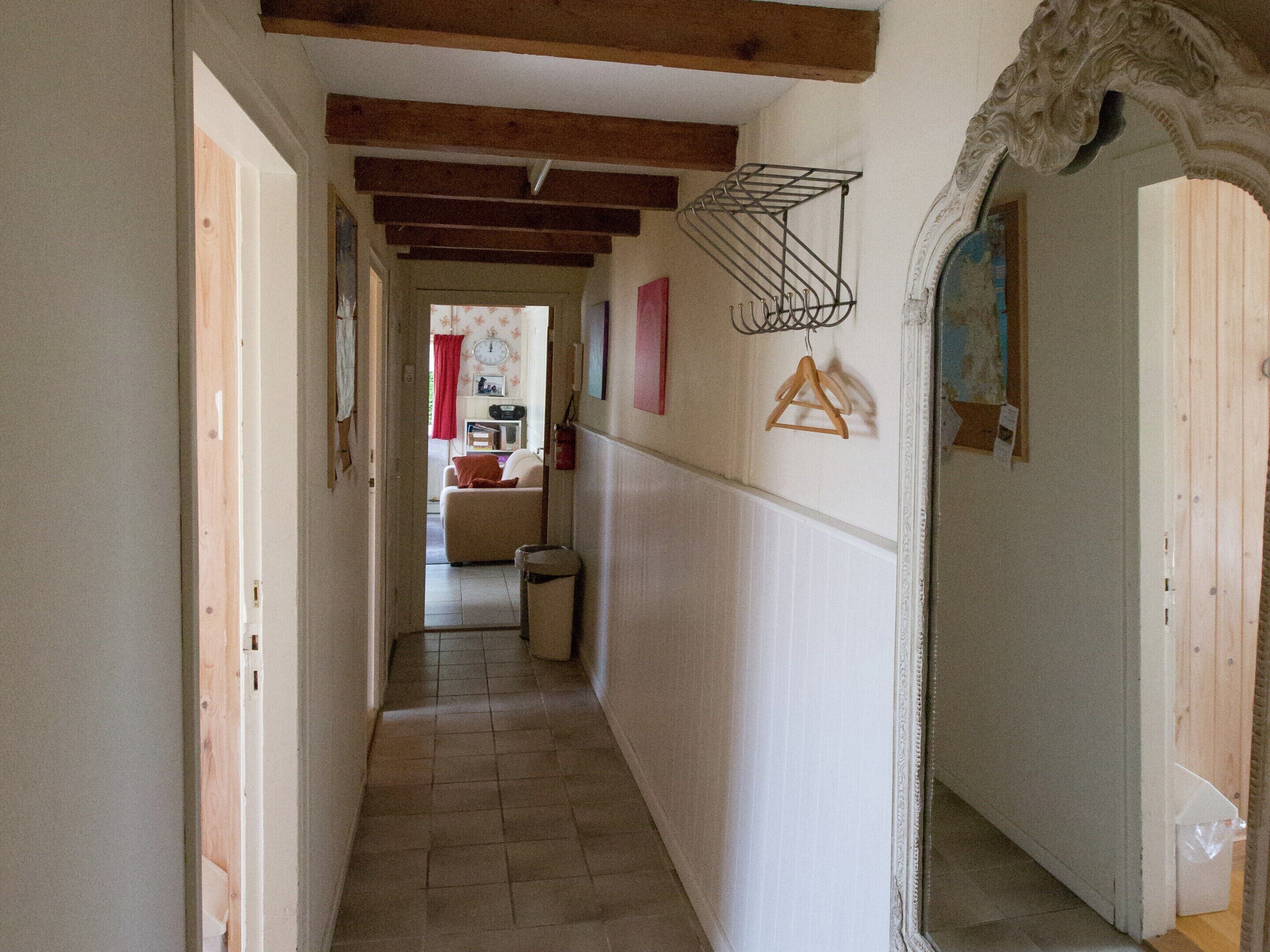 Un pasillo estrecho con suelo de baldosas, vigas de madera en el techo, un tendedero de metal y una puerta con un marco decorativo.