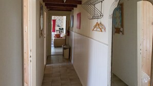 A narrow hallway with a tiled floor, wooden beams on the ceiling, a metal drying rack, and a door with an ornate frame.