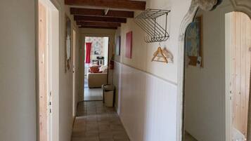 Un pasillo estrecho con suelo de baldosas, vigas de madera en el techo, un tendedero de metal y una puerta con un marco decorativo.