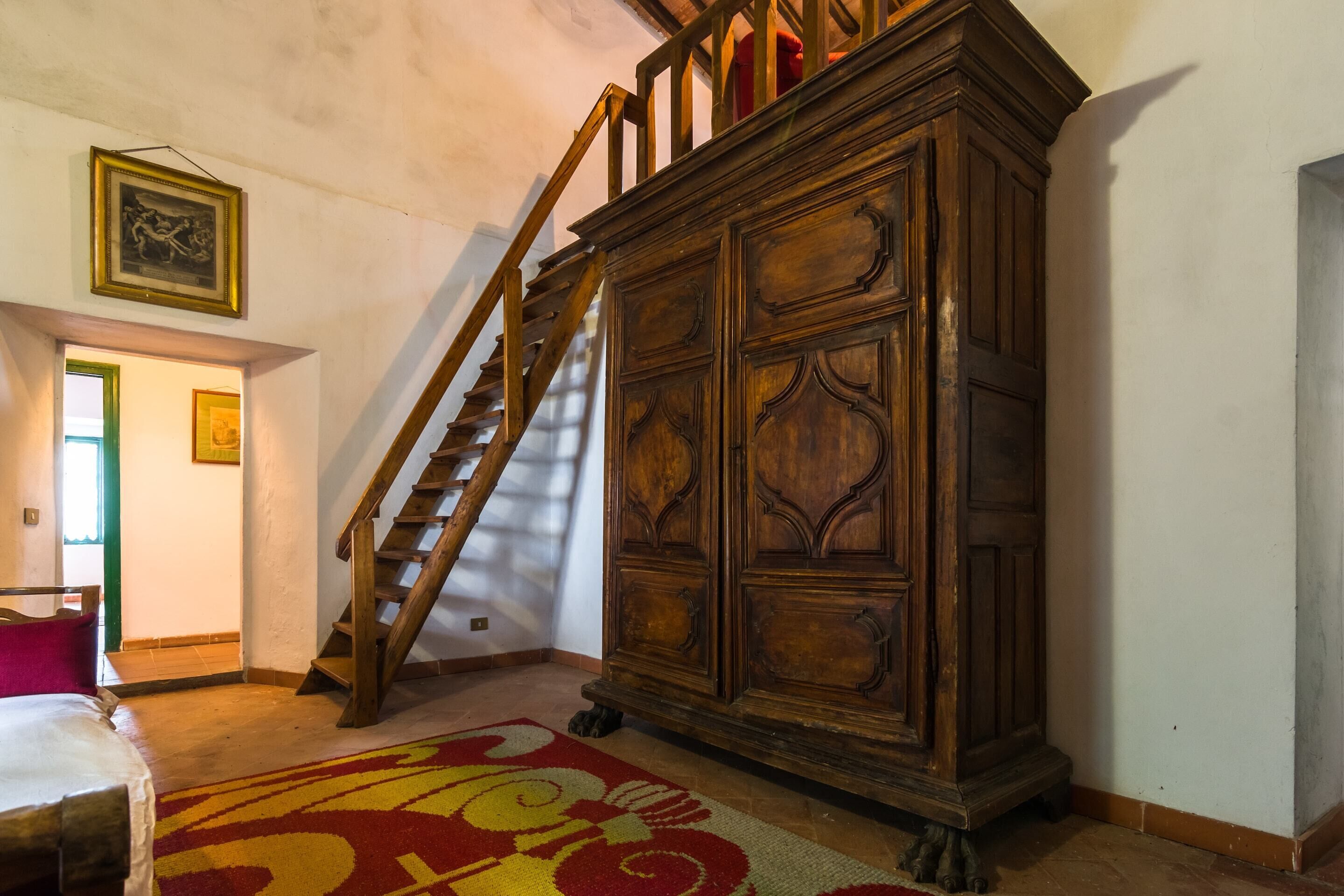 Ein Zimmer mit einer Holztreppe, einem großen Schrank und einem gemusterten Teppich.
