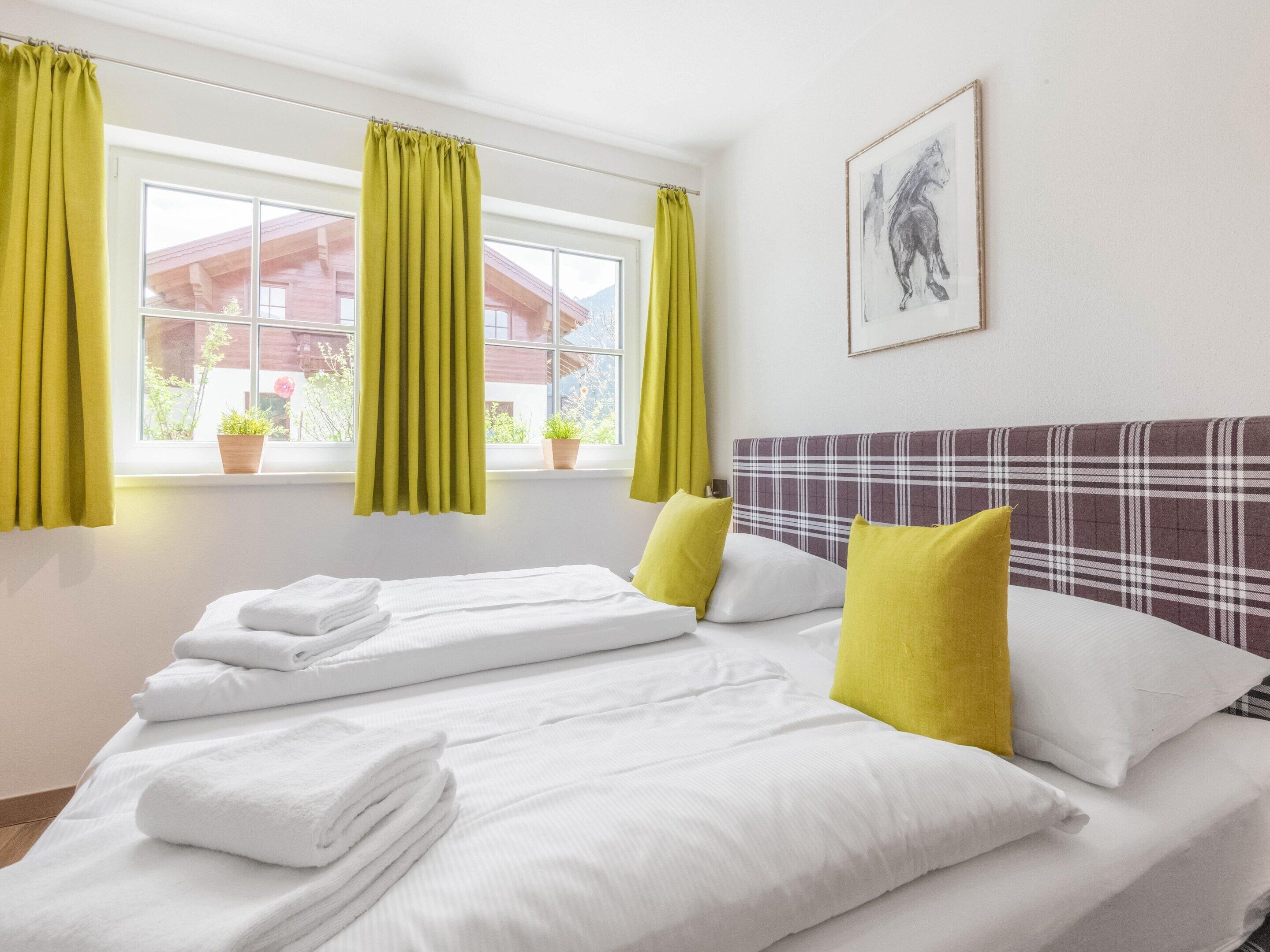 A hotel room with two beds, a plaid headboard, a window with curtains, and a framed picture on the wall.