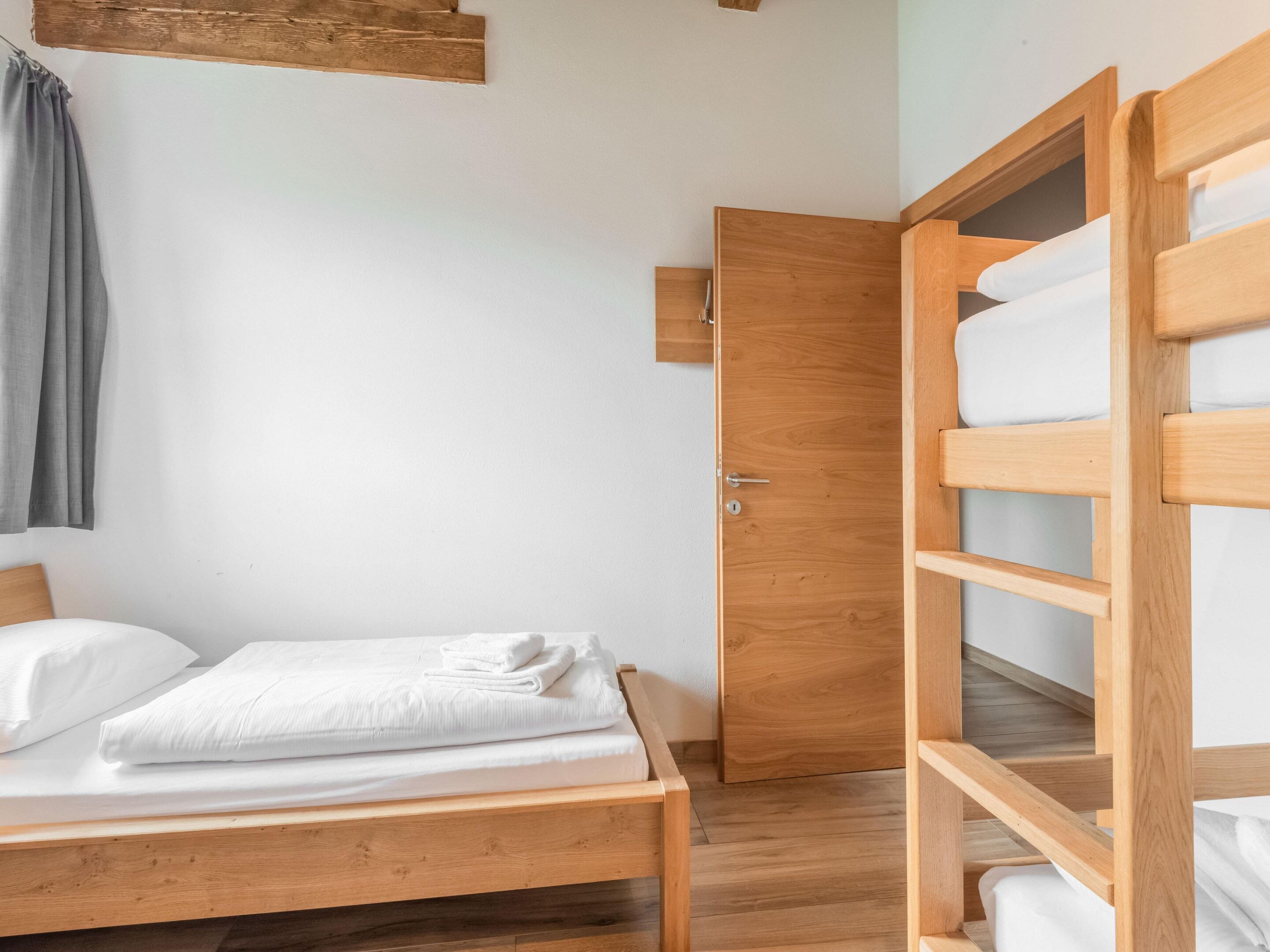 Une chambre avec un lit superposé en bois, un lit simple et une porte en bois.