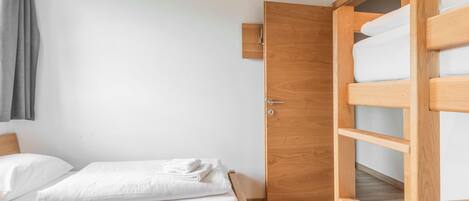 Une chambre avec un lit superposé en bois, un lit simple et une porte en bois.