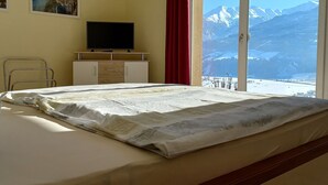 Ett hotellrum med en säng, en tv på ett skåp och utsikt över snöklädda berg genom en skjutdörr.