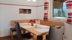 A dining area with a wooden table, chairs, a bench, and a window with curtains. - Apartment in Zillertal Near Ski Slopes (Fuegenberg)