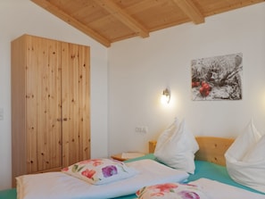 Quarto com guarda-roupa de madeira, cama com almofadas florais, mesa de cabeceira e luminária na parede.