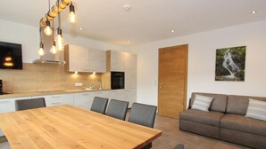 A modern kitchen with a wooden dining table and chairs, a grey sofa, and a mounted TV. - Luxurious Apartment in Fugenberg With Sauna (Fuegenberg)