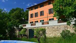 A multi-story building with a stone base and a flat roof, surrounded by greenery. - Hillside Villa in the Heart of Chianti (San Casciano in Val di Pesa)