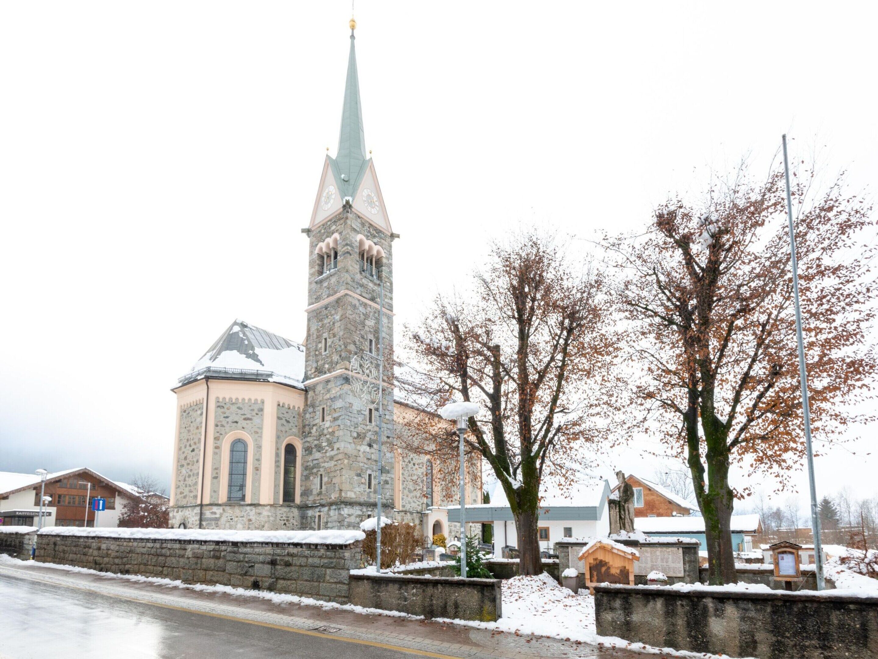 Eine Kirche mit hohem Turm und Kuppel, umgeben von schneebedeckten Bäumen und Gebäuden.