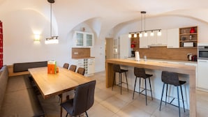 Una cocina moderna con una isla de madera, armarios blancos y un horno empotrado. Hay una zona de comedor con un banco y sillas.