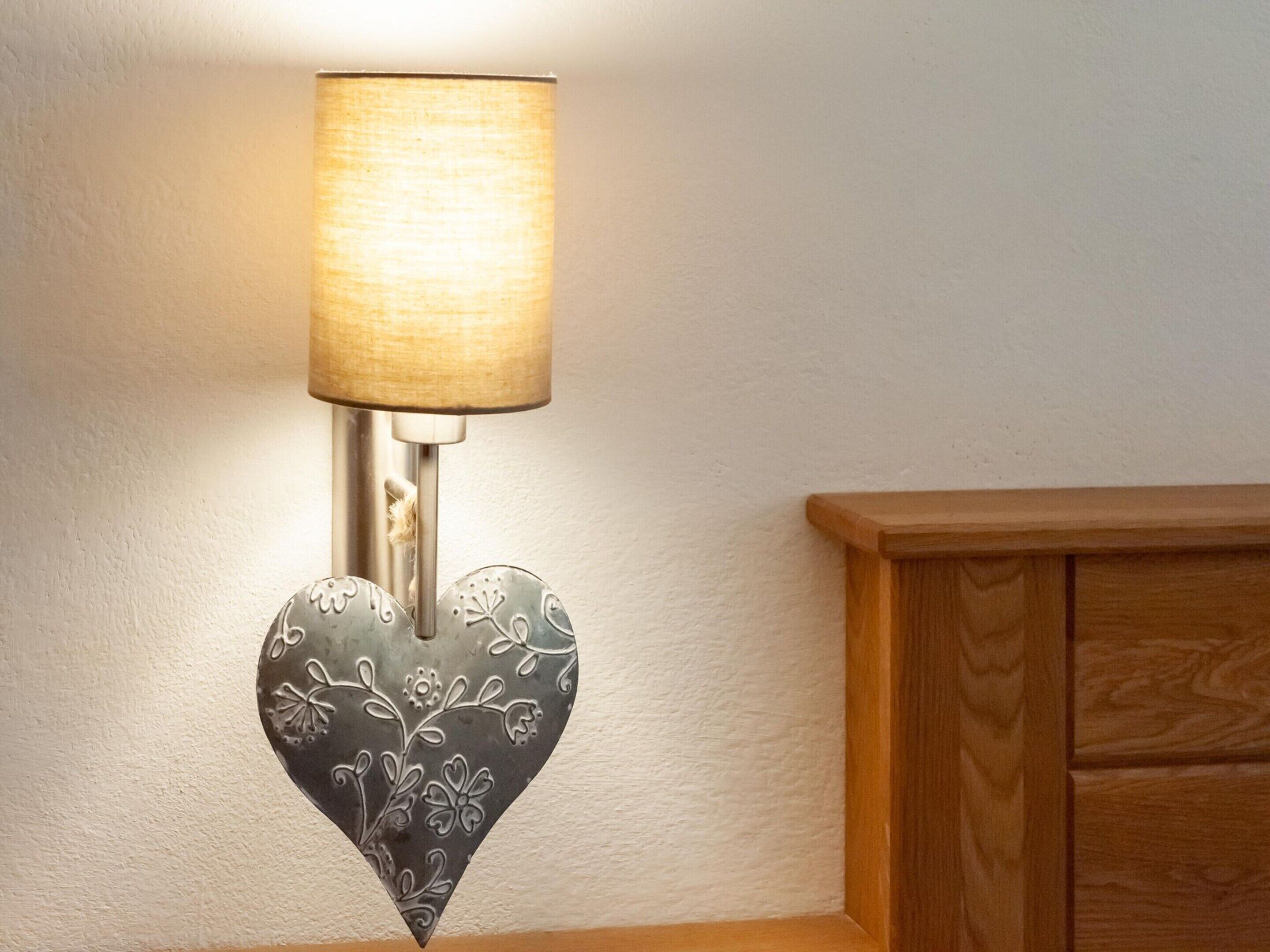 A wall-mounted lamp with a heart-shaped metal base and a cylindrical shade.