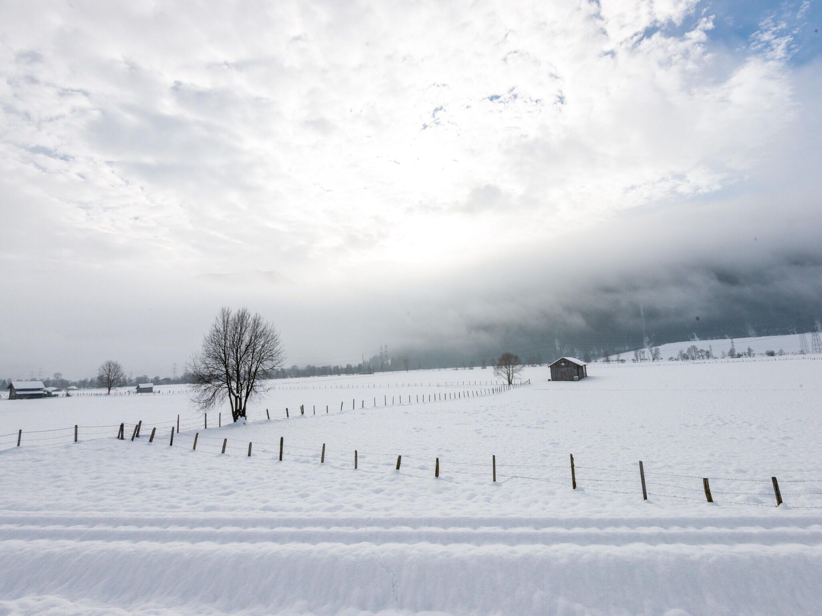 A snow-covered field with a wooden fence and a small building in the distance.