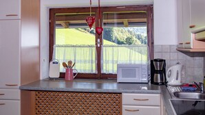 Una cocina con ventana, microondas, hervidor y pileta.