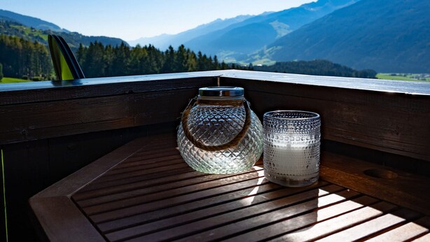 Una mesa de madera con dos recipientes de vidrio en un balcón con vista a un paisaje montañoso.